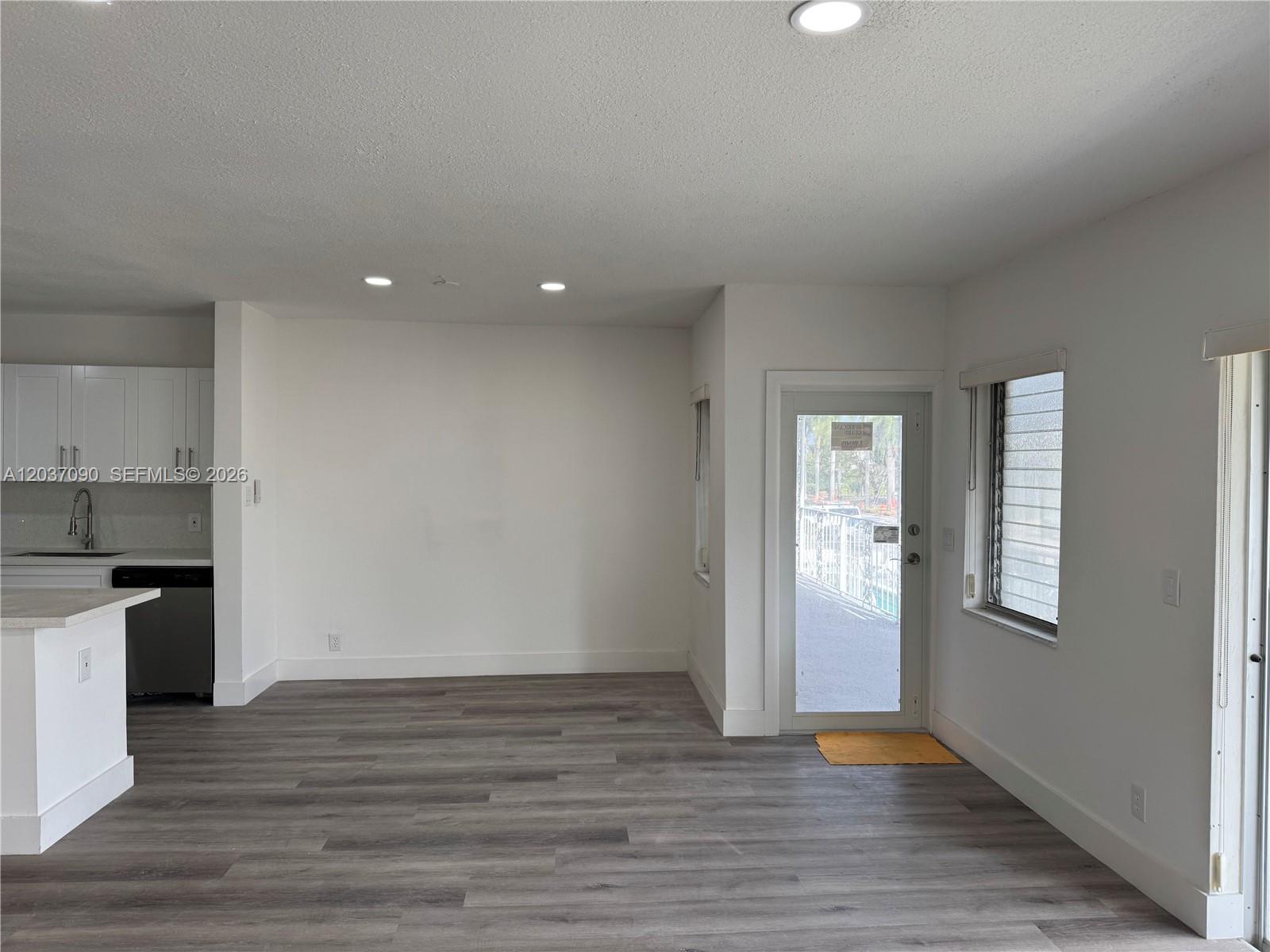 An open-concept room features gray wood-look flooring, white walls, recessed lighting, and a glass door — 630 Layne Blvd # 211, Hallandale Beach FL 33009, HALLANDALE BEACH, FL