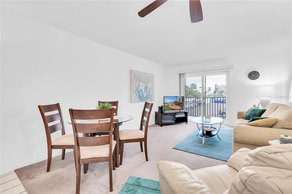 A living and dining area features a glass-top table, beige sofa, and sliding glass doors — 10365 PARADISE BOULEVARD UNIT 4, TREASURE ISLAND, FL