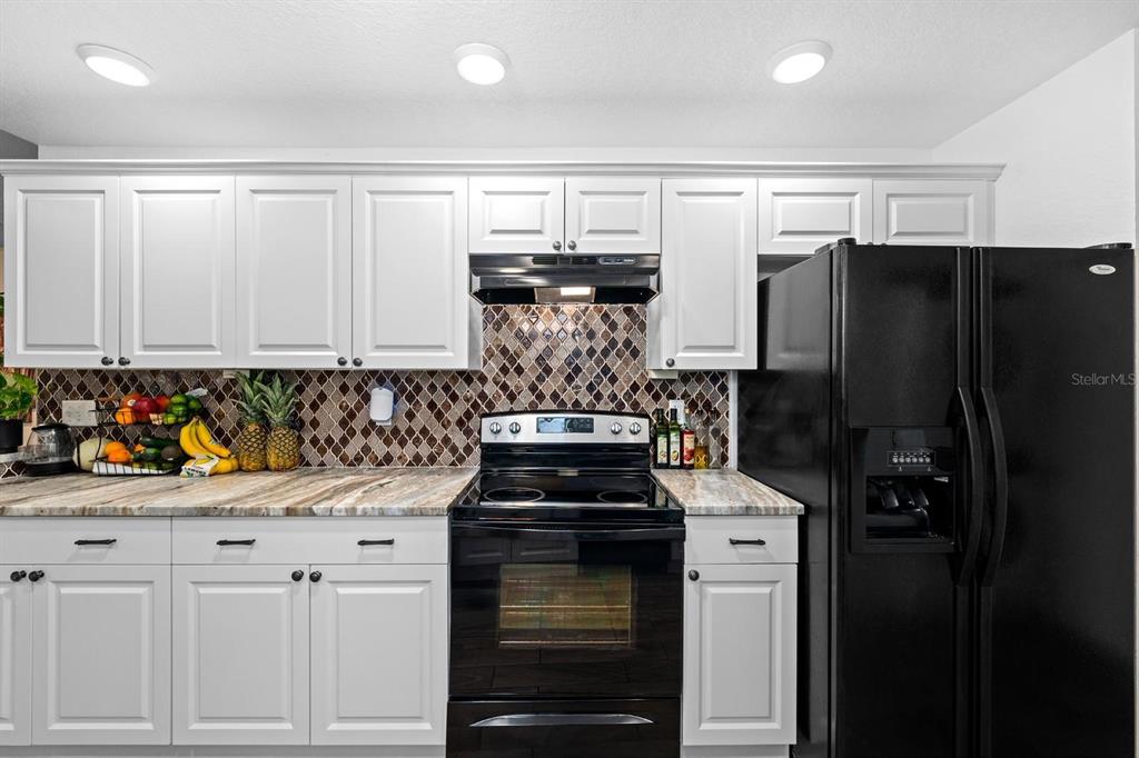 A kitchen features white cabinets, a black stove, a black refrigerator, and a mosaic backsplash — 2563 13TH AVENUE S, ST PETERSBURG, FL