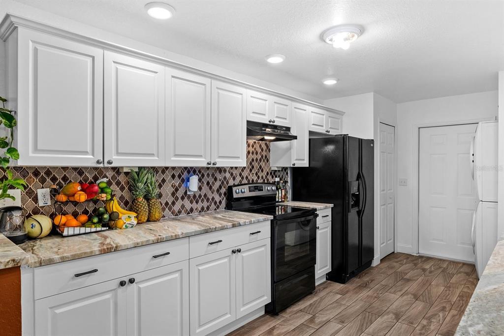 A kitchen features white cabinets, granite countertops, a mosaic tile backsplash, and black appliances — 2563 13TH AVENUE S, ST PETERSBURG, FL