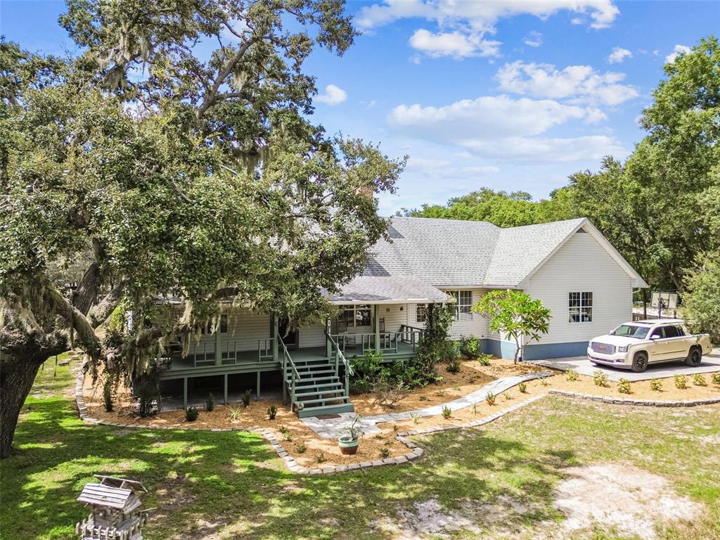 A white house with a wrap-around porch sits among large trees with a parked truck — 15019 CARLTON LAKE ROAD, WIMAUMA, FL