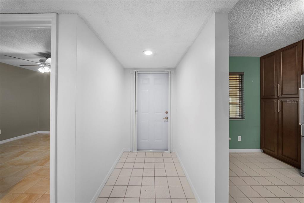 A tiled entryway leads to a white front door, flanked by a kitchen and living area — 7761 JEWEL LANE UNIT 102, NAPLES, FL