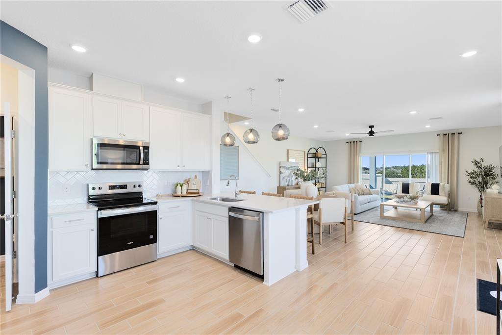 A modern open-concept kitchen with white cabinets, stainless steel appliances, and light wood flooring — 4364 CHESTER SPRINGS BOULEVARD, DAVENPORT, FL