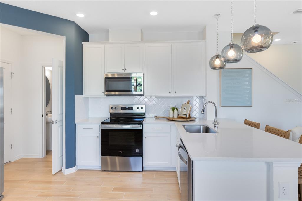 A modern kitchen features white cabinetry, stainless steel appliances, quartz countertops, and light wood flooring — 4364 CHESTER SPRINGS BOULEVARD, DAVENPORT, FL