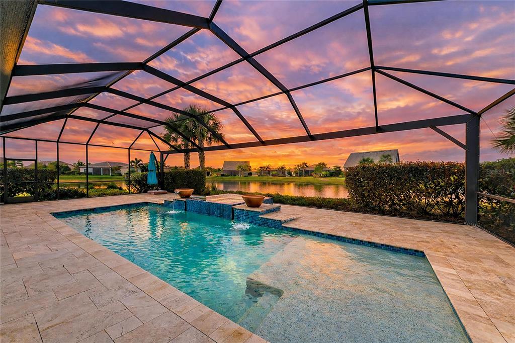 A screened-in swimming pool with a water feature overlooks a lake at sunset — 7110 GRADFORD COURT, LAKEWOOD RANCH, FL