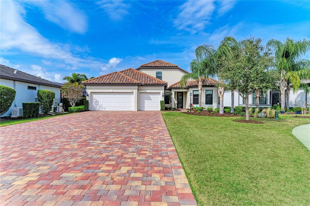 A single-family home with a brick paver driveway, a three-car garage, and palm trees — 7110 GRADFORD COURT, LAKEWOOD RANCH, FL