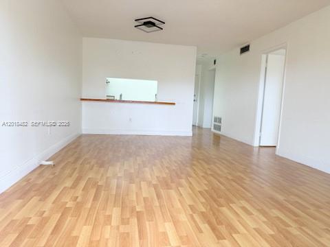 An empty living room with light wood-look flooring and a kitchen pass-through window — 7815 Camino Real # i417, Miami FL 33143, MIAMI, FL