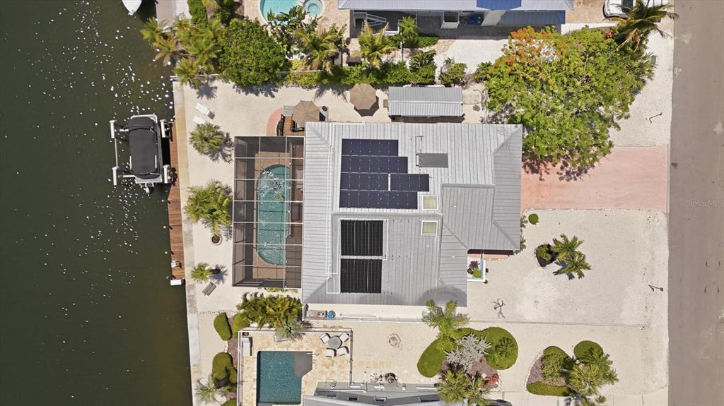 An aerial view shows a house with solar panels and a pool cage by water — 517 KUMQUAT DRIVE, ANNA MARIA, FL