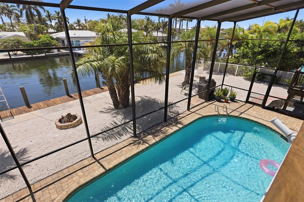 A screened-in pool area overlooks a canal with a gravel patio and a fire pit — 517 KUMQUAT DRIVE, ANNA MARIA, FL