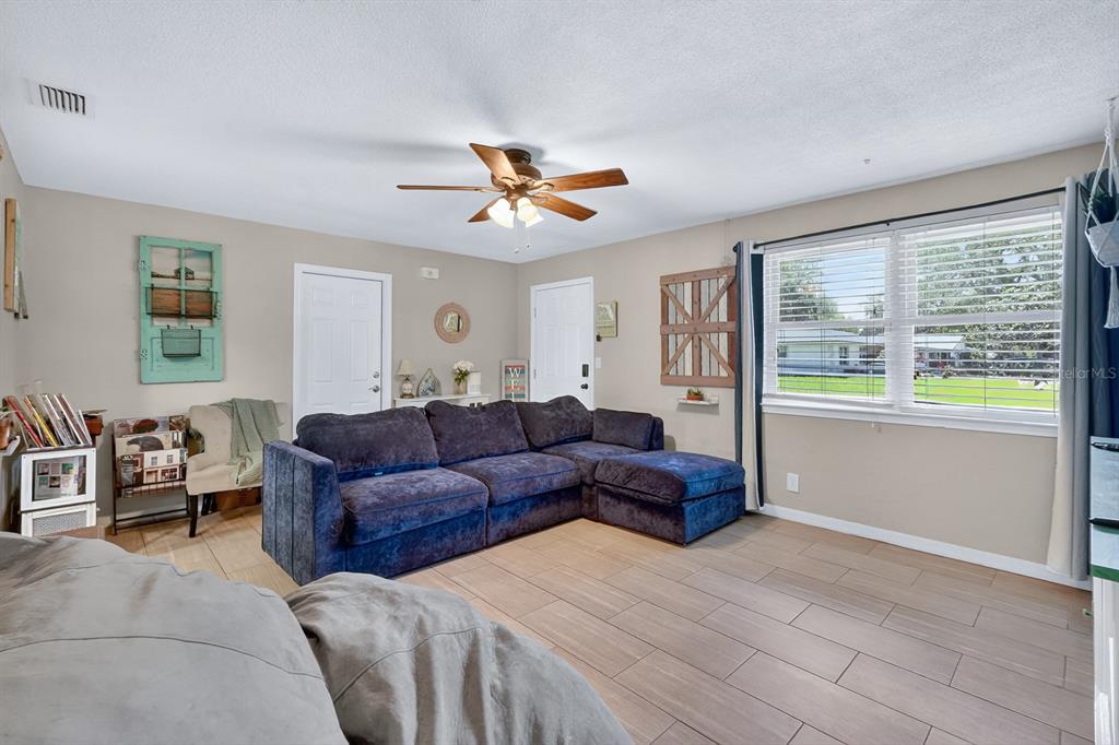 A living room features a blue sectional sofa, wood-look tile floors, and a ceiling fan — 327 LONDON ROAD, DAYTONA BEACH, FL