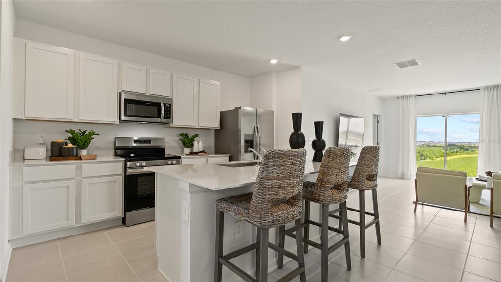 A kitchen with white cabinets, stainless steel appliances, and an island with three wicker stools — 6225 BOTTICELLA BOULEVARD, WINTER HAVEN, FL
