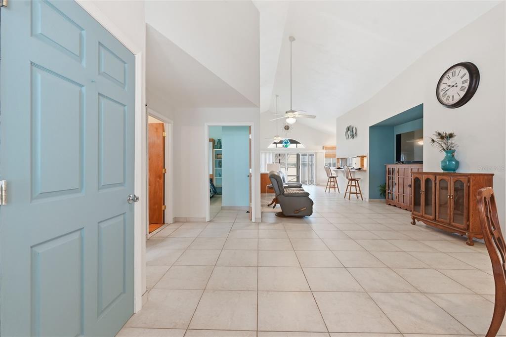 A bright, open-concept living area features vaulted ceilings, light tile flooring, and a blue door — 585 SELLARS DRIVE, LAKE ALFRED, FL