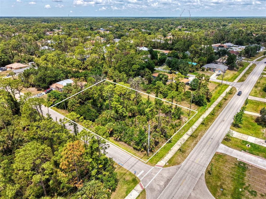 An aerial view shows a vacant, tree-covered corner lot outlined in white — FONSICA AVENUE, NORTH PORT, FL