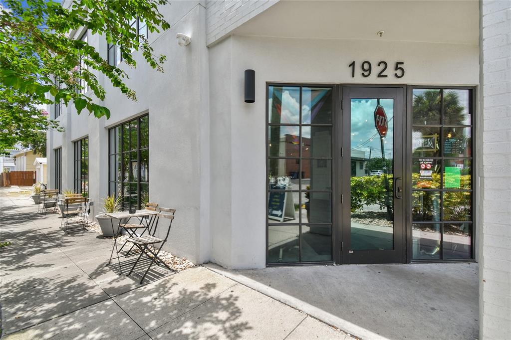 The exterior of a white building features a glass entrance door and outdoor seating — 1919 E 6TH AVENUE, TAMPA, FL
