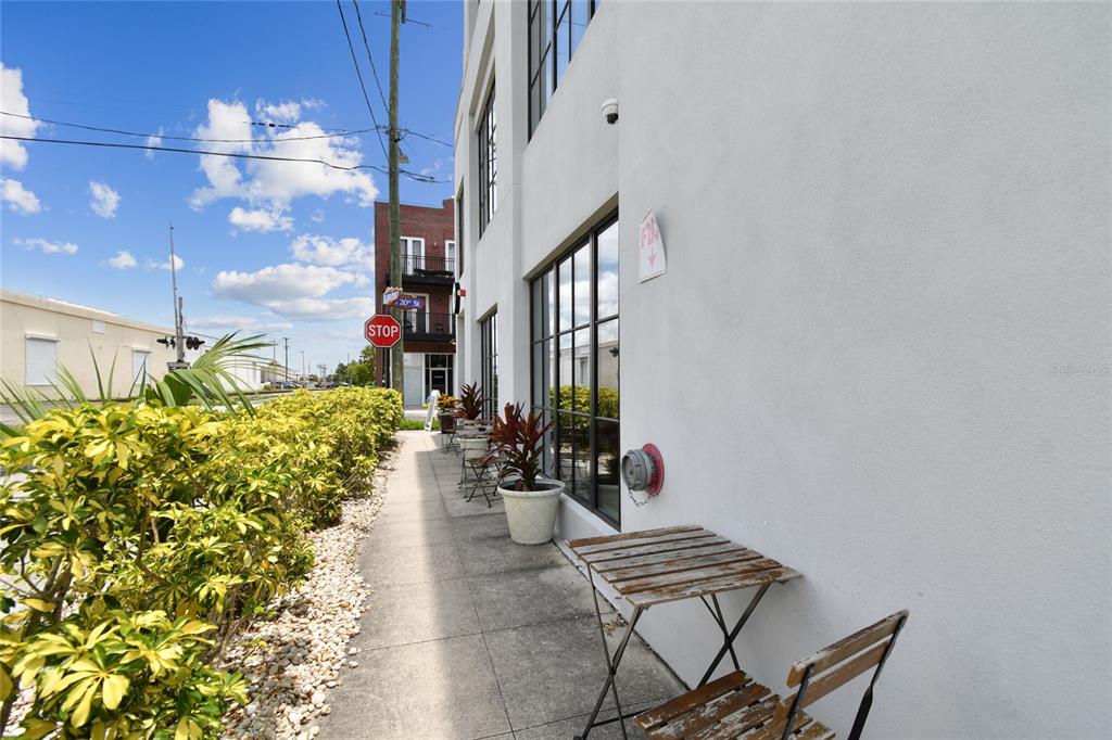 A sidewalk runs alongside a white building exterior with outdoor seating and a stop sign — 1919 E 6TH AVENUE, TAMPA, FL