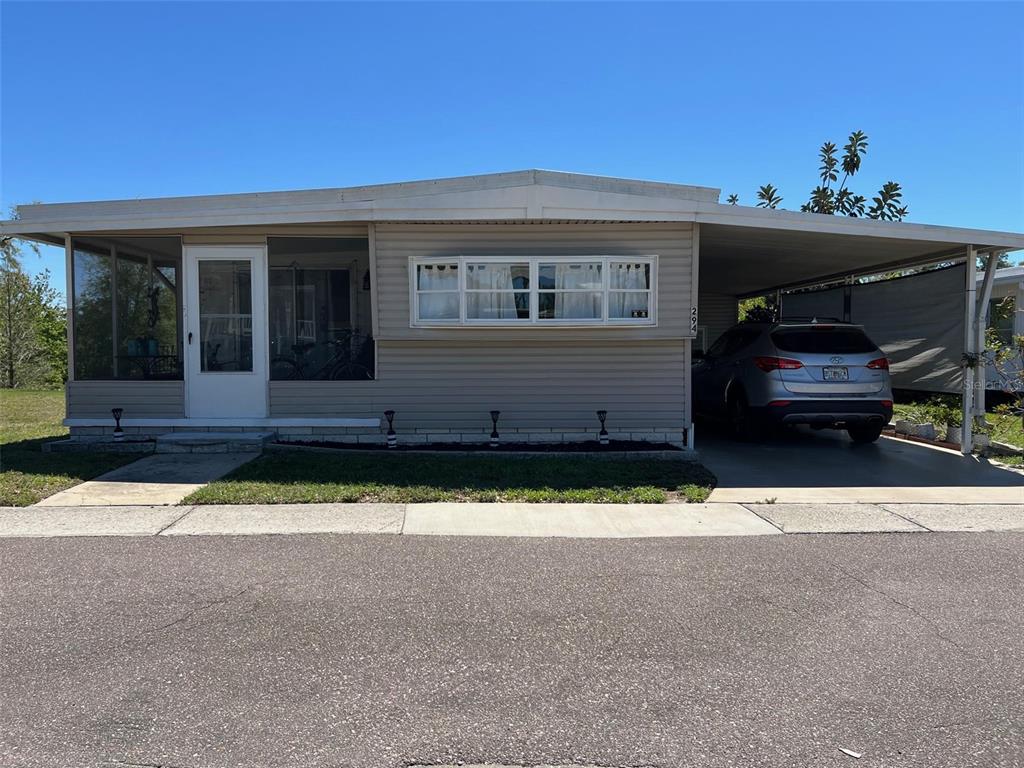 A single-story manufactured home features a screened-in porch, a carport, and light-colored horizontal siding — 29250 US HIGHWAY 19 N UNIT 294, CLEARWATER, FL