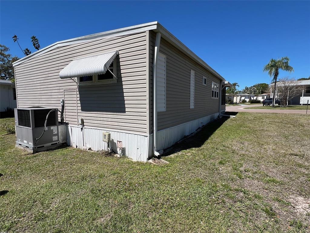 The exterior of a tan manufactured home features horizontal siding, a metal window awning, and an HVAC unit — 29250 US HIGHWAY 19 N UNIT 294, CLEARWATER, FL