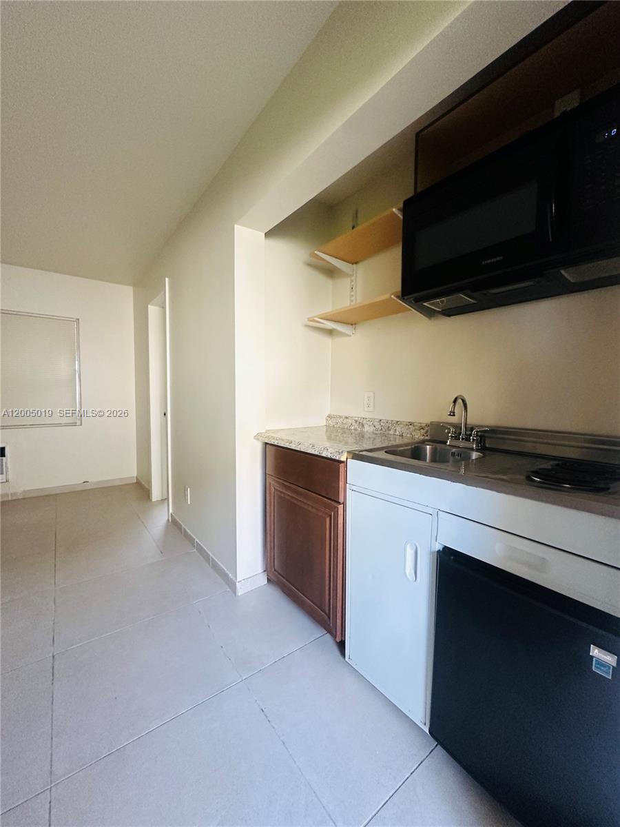 A small kitchenette features a sink, microwave, open shelving, and a compact refrigerator — 1708 Van Buren St # 3, Hollywood FL 33020, HOLLYWOOD, FL