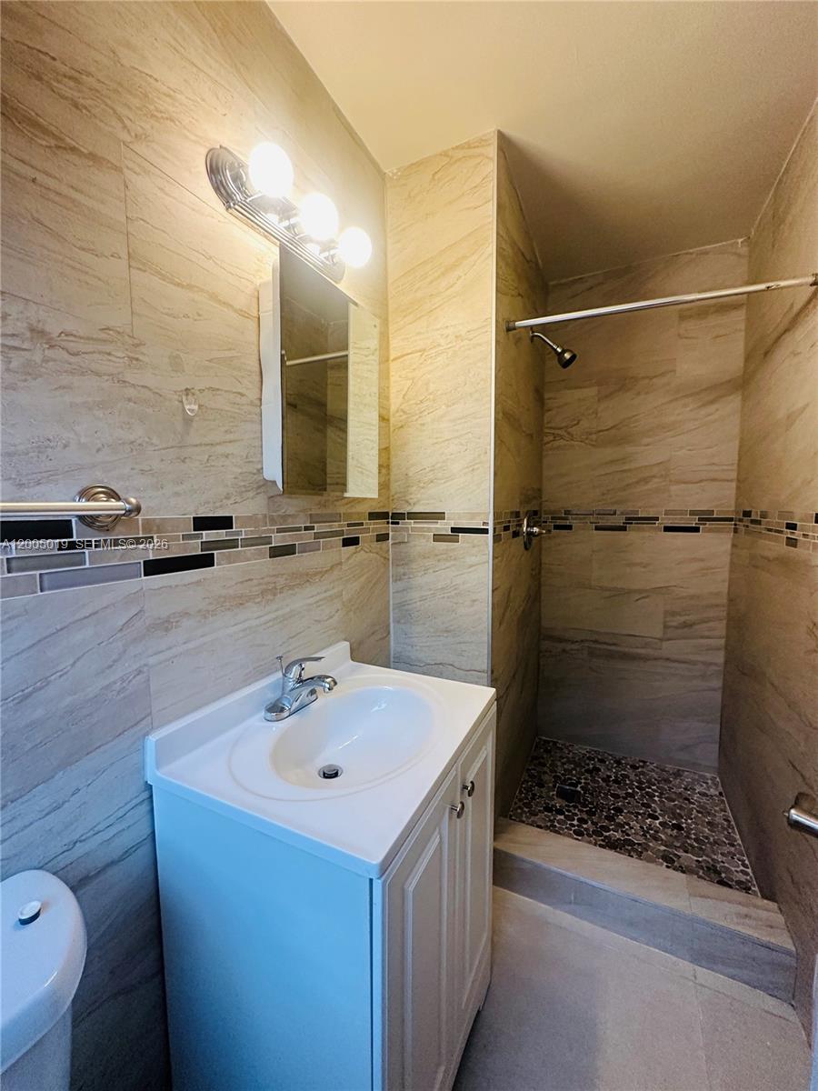 A bathroom features a white vanity, a walk-in shower with pebble flooring, and beige tiling — 1708 Van Buren St # 3, Hollywood FL 33020, HOLLYWOOD, FL