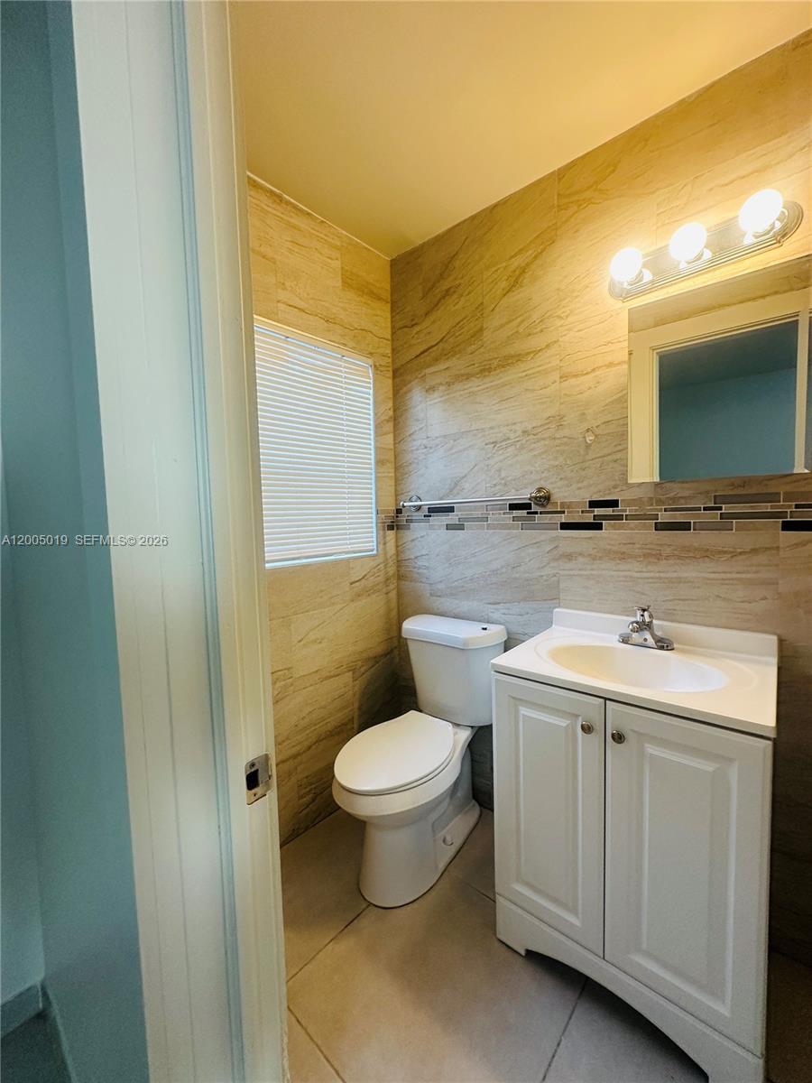A bathroom features beige tiled walls, a white vanity, a toilet, and a vanity light — 1708 Van Buren St # 3, Hollywood FL 33020, HOLLYWOOD, FL