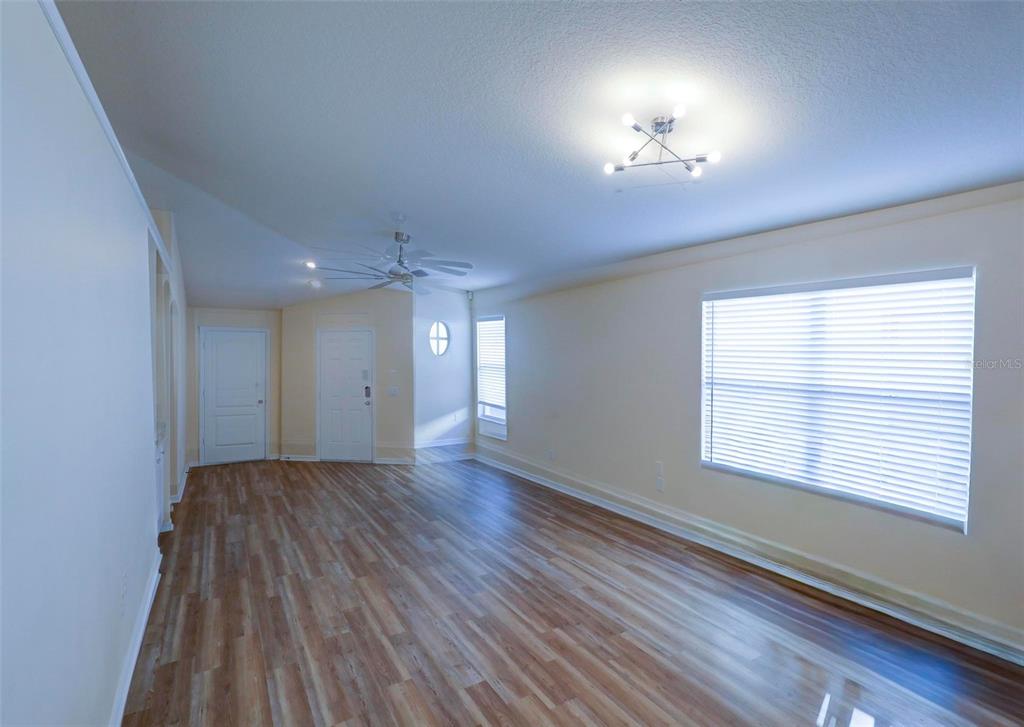 An empty room features light wood-look flooring, white walls, a ceiling fan, and large windows — 18105 LEMBRECHT WAY, TAMPA, FL