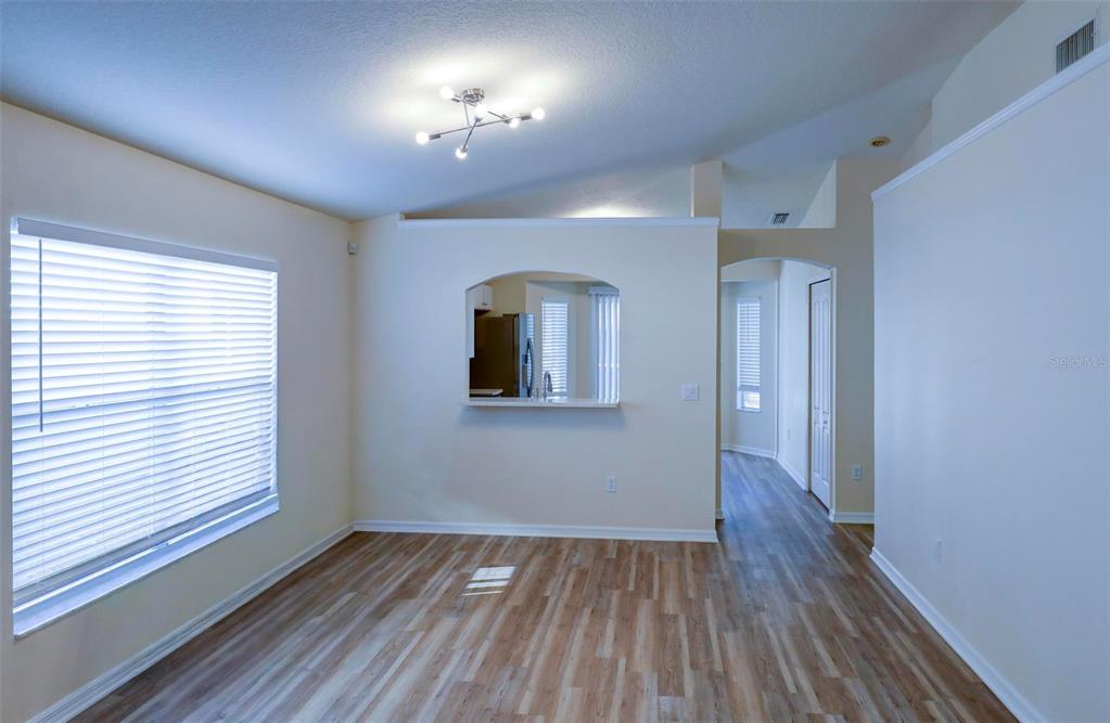 An empty room with wood-look flooring, a pass-through window to the kitchen, and a ceiling light — 18105 LEMBRECHT WAY, TAMPA, FL