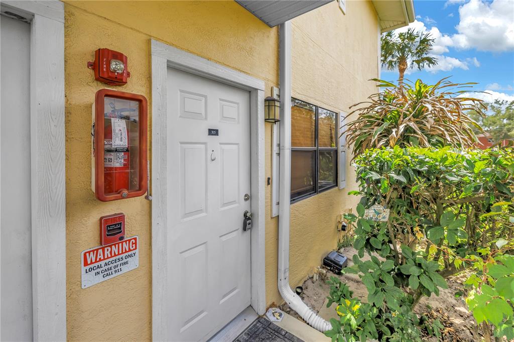 An exterior view of a building entrance with a white door, fire extinguisher, and signage — 3001 58TH AVENUE S UNIT 315, ST PETERSBURG, FL