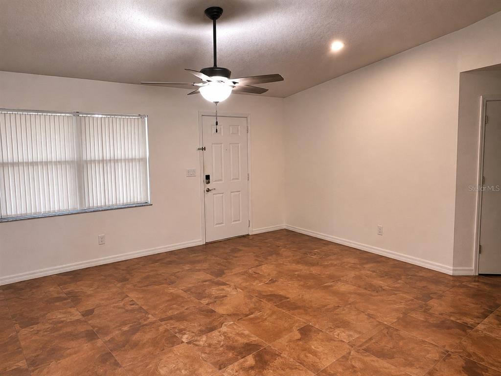 An empty room features brown tile flooring, a ceiling fan, and a white entry door — 3665 SE 137TH LANE, SUMMERFIELD, FL