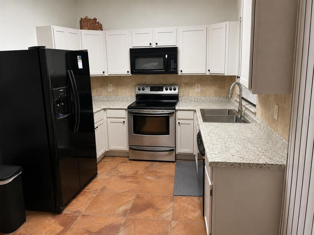 A kitchen features white cabinets, granite countertops, stainless steel appliances, and brown tile flooring — 3665 SE 137TH LANE, SUMMERFIELD, FL