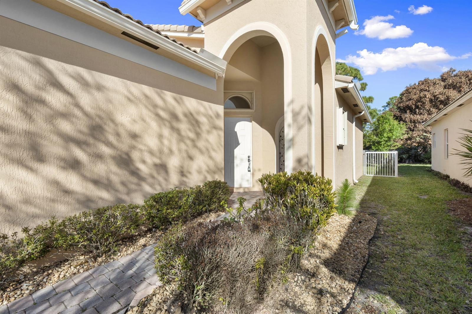 A beige stucco house features an arched entryway, a white front door, and a walkway — 5627 Sunberry Circle, Fort Pierce FL 34951, FORT PIERCE, FL