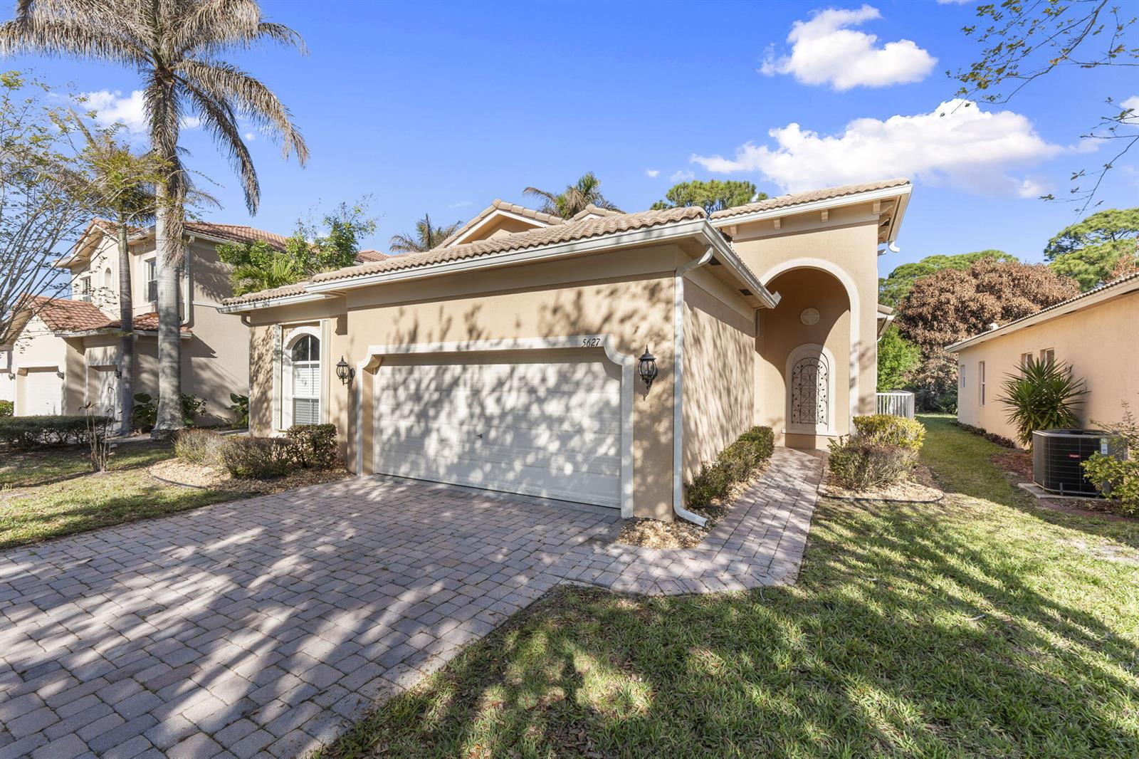 A beige single-story house with a two-car garage and a paved driveway under a blue sky — 5627 Sunberry Circle, Fort Pierce FL 34951, FORT PIERCE, FL