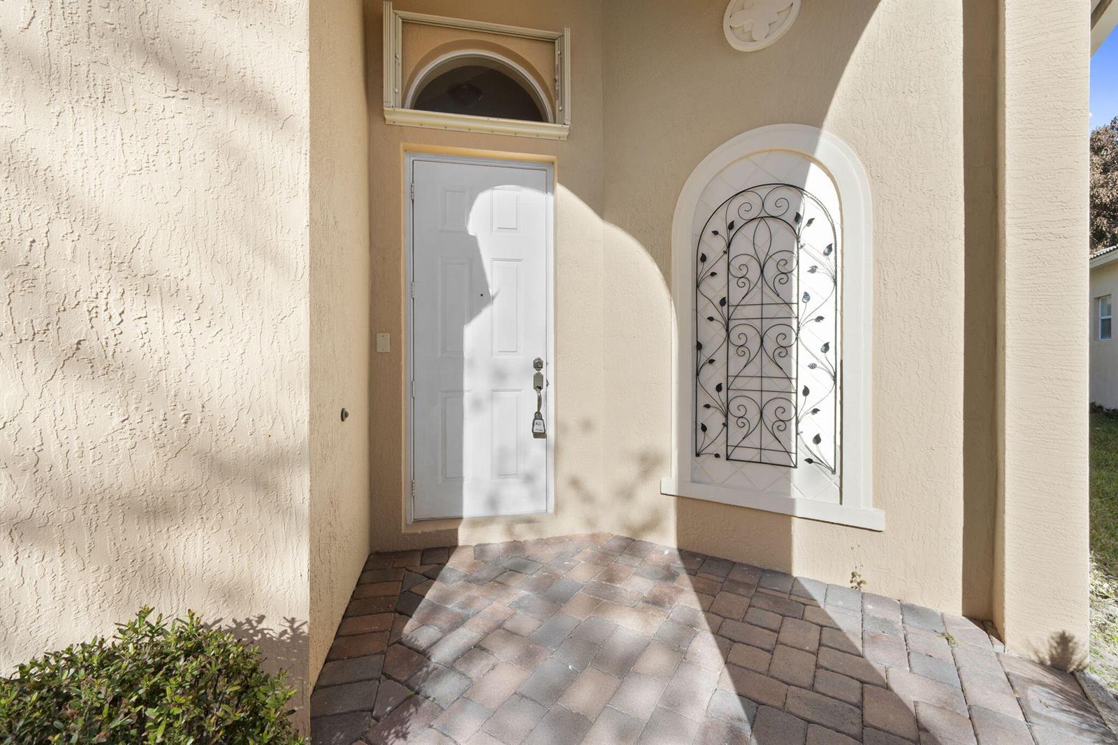 A white front door with a decorative metal wall insert sits on a paved entryway — 5627 Sunberry Circle, Fort Pierce FL 34951, FORT PIERCE, FL