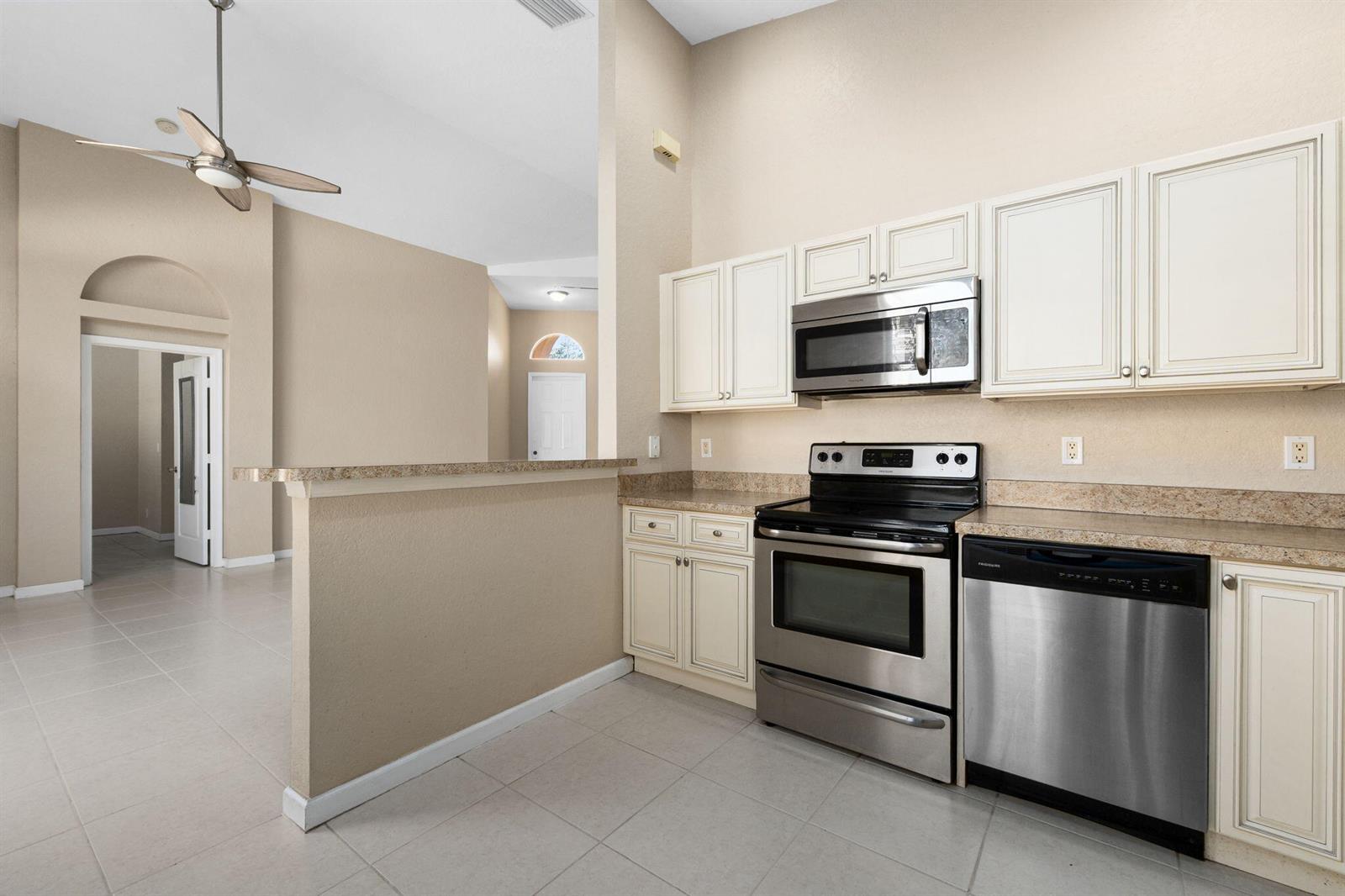 A kitchen features stainless steel appliances, off-white cabinets, and a breakfast bar overlooking a room — 5627 Sunberry Circle, Fort Pierce FL 34951, FORT PIERCE, FL