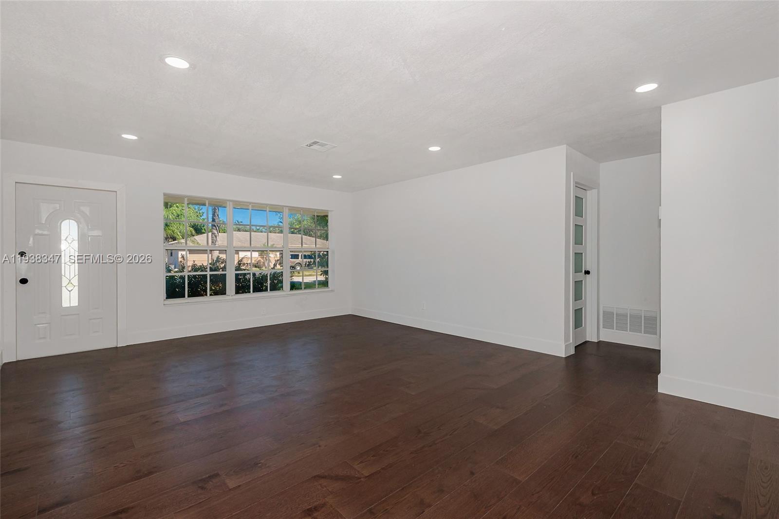A bright, empty room features dark wood flooring, white walls, recessed lighting, and a window — 4360 NW 4th St, Plantation FL 33317, PLANTATION, FL