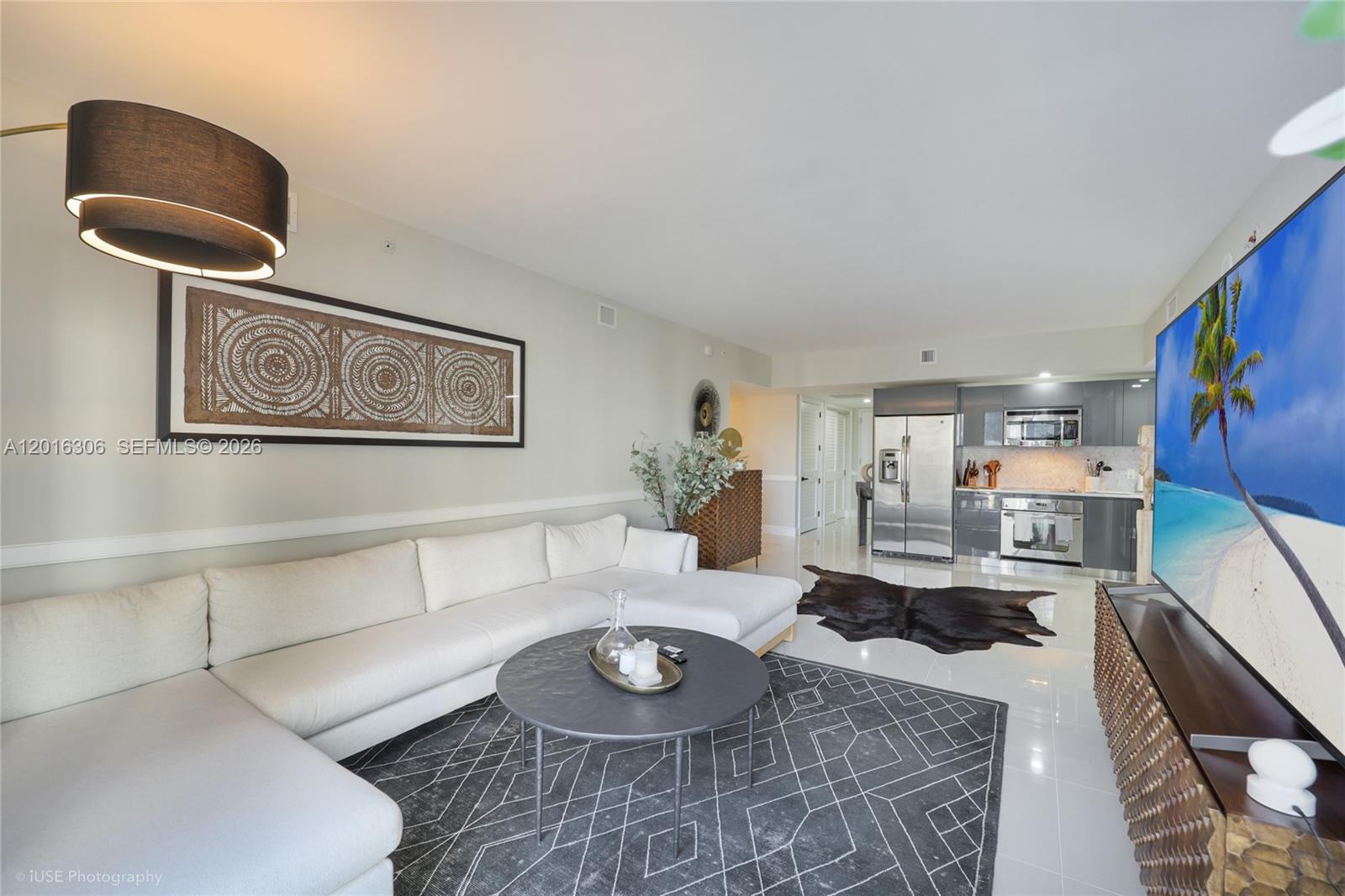 A living room with a white sectional, patterned rug, and an open kitchen with appliances — 31 SE 6th St # 2207, Miami FL 33131, MIAMI, FL