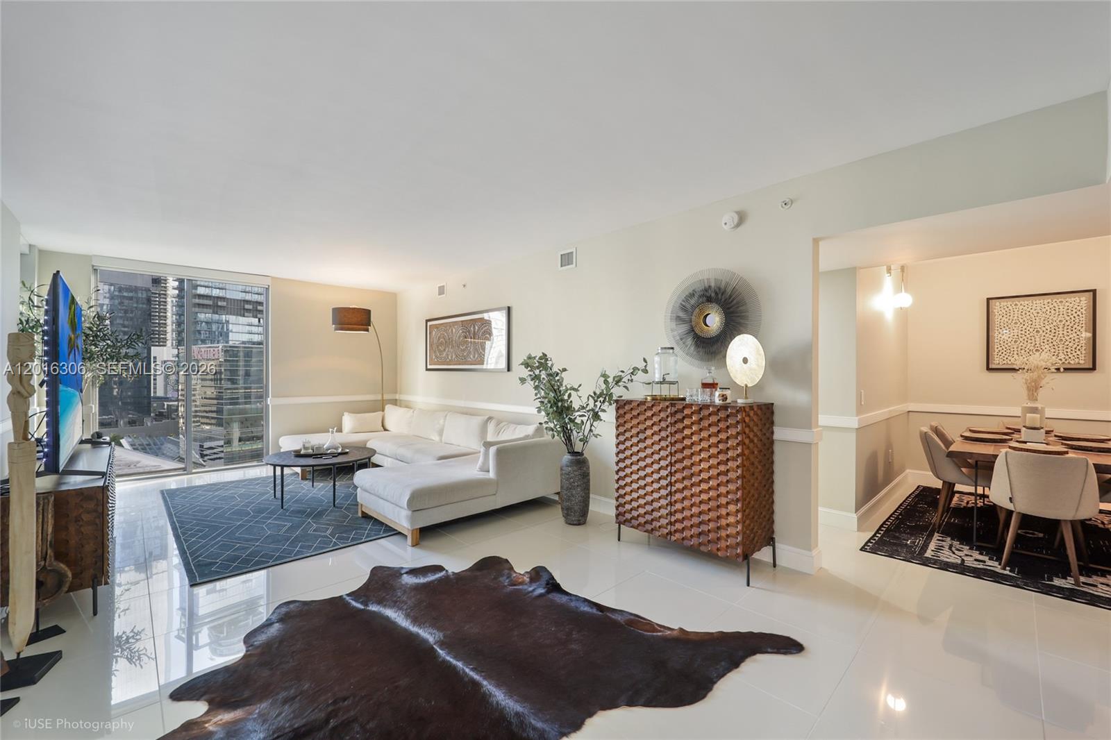 A modern living and dining area features white tile floors, a sectional sofa, and city views — 31 SE 6th St # 2207, Miami FL 33131, MIAMI, FL