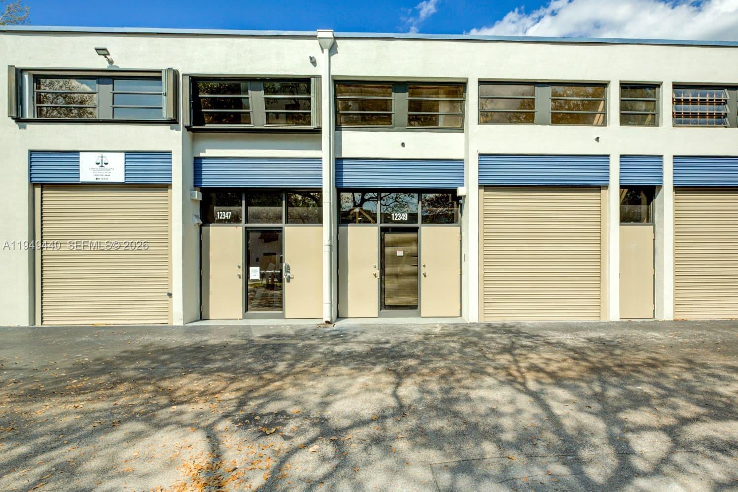 The exterior of a commercial building features multiple roll-up garage doors and glass entryways — 12349 SW 132nd Ct # 9, Miami FL 33186, MIAMI, FL