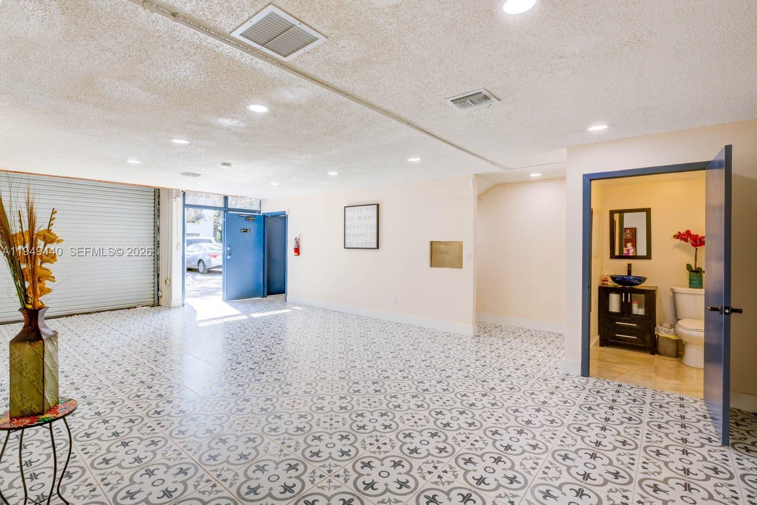 A large room with patterned tile flooring, recessed lighting, a roll-up door, and a bathroom — 12349 SW 132nd Ct # 9, Miami FL 33186, MIAMI, FL