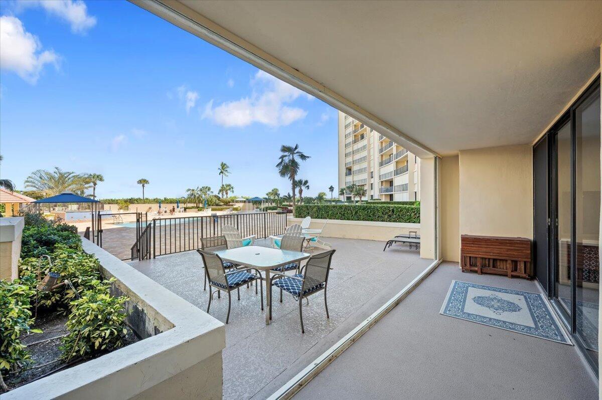 A covered patio features a dining set overlooking a swimming pool and a tall building — 100 Ocean Trail Way # 107, Jupiter FL 33477, JUPITER, FL