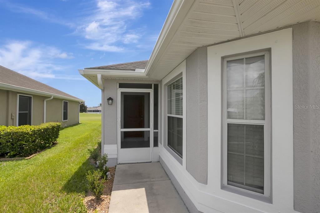 A gray house exterior features a concrete walkway leading to a screened-in front entryway — 7088 WIREVINE DRIVE, BROOKSVILLE, FL