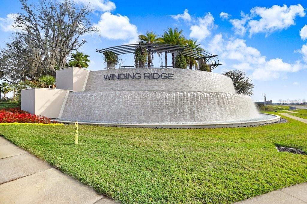 A curved stone water feature displays the Winding Ridge community name under a metal trellis — 3281 GREAT BANYAN WAY, WESLEY CHAPEL, FL
