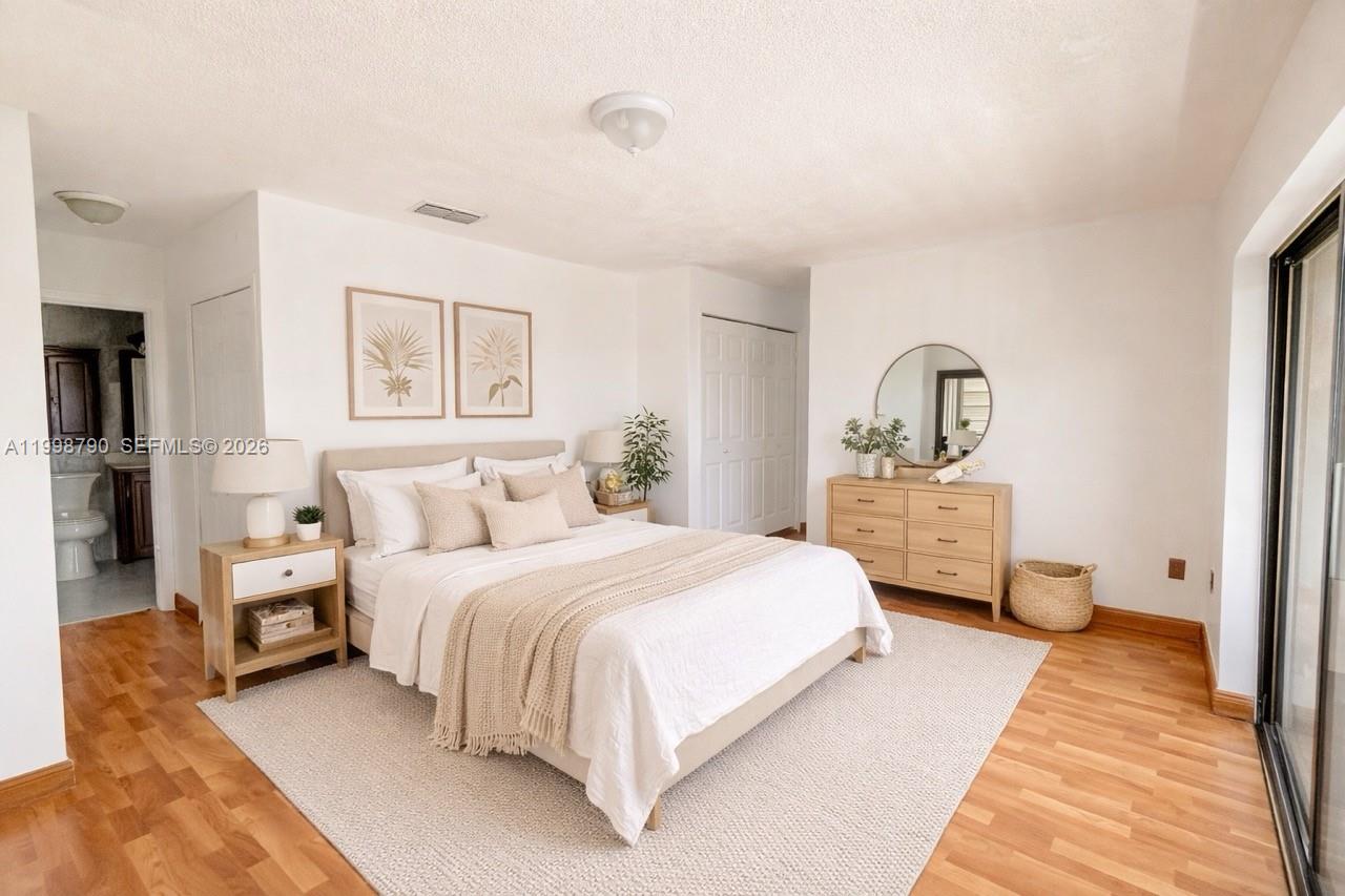 A bedroom features a bed, light wood furniture, a round mirror, and wood-look flooring — 1283 W 51st Place # 12, Hialeah FL 33012, HIALEAH, FL