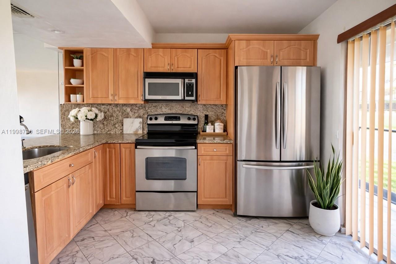 A kitchen features light wood cabinets, stainless steel appliances, granite countertops, and marble-patterned tile flooring — 1283 W 51st Place # 12, Hialeah FL 33012, HIALEAH, FL