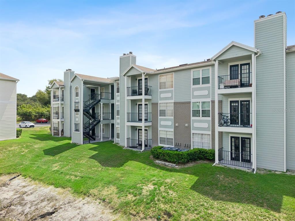 A three-story apartment building with light green siding, brick accents, and exterior staircases — 2550 N ALAFAYA TRAIL UNIT 7203, ORLANDO, FL