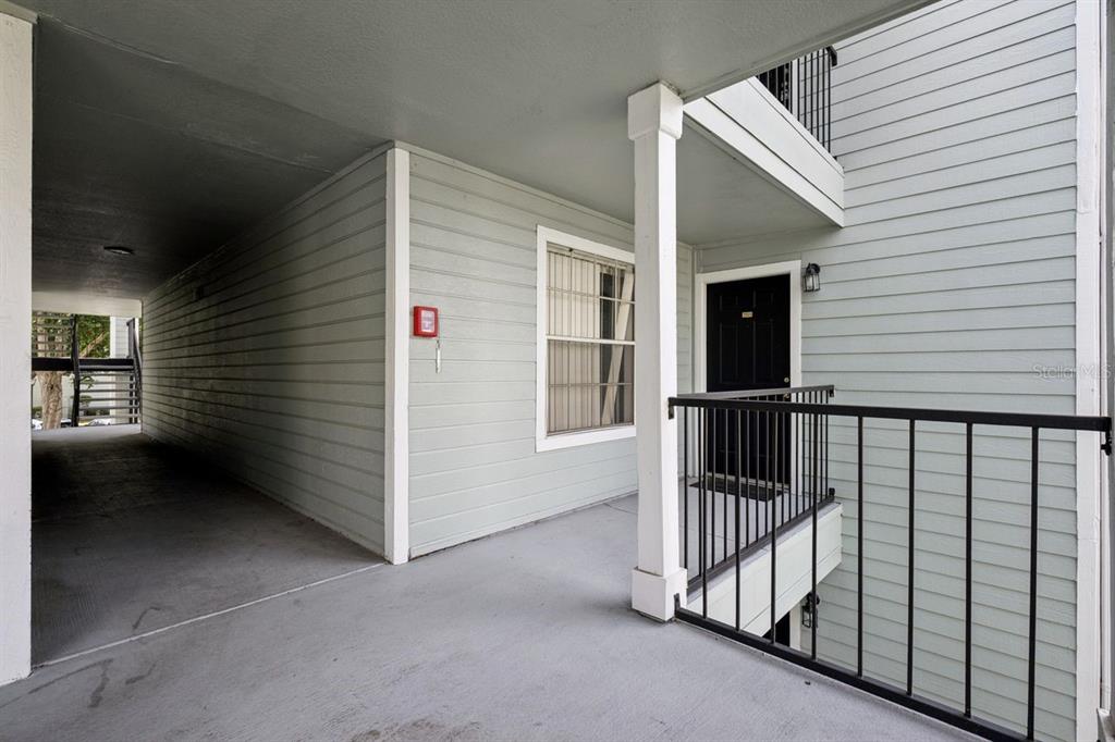 An outdoor apartment walkway with light gray siding, a black door, and a metal railing — 2550 N ALAFAYA TRAIL UNIT 7203, ORLANDO, FL