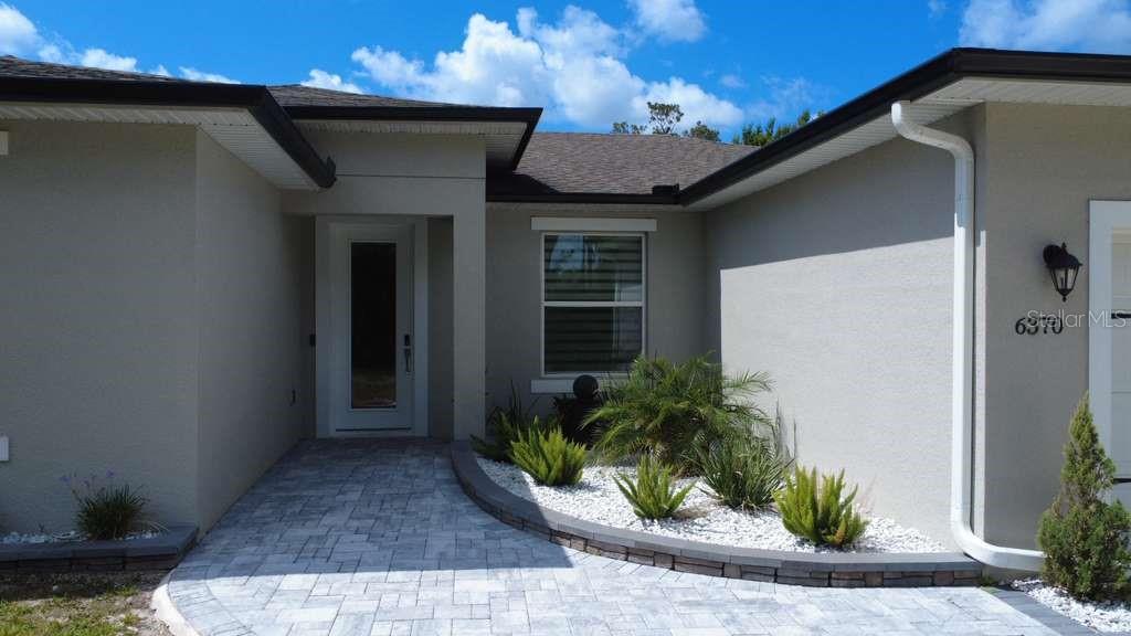 The exterior of a house features a paved walkway, a white front door, and landscaping — 6370 BENNETT COURT, ST CLOUD, FL