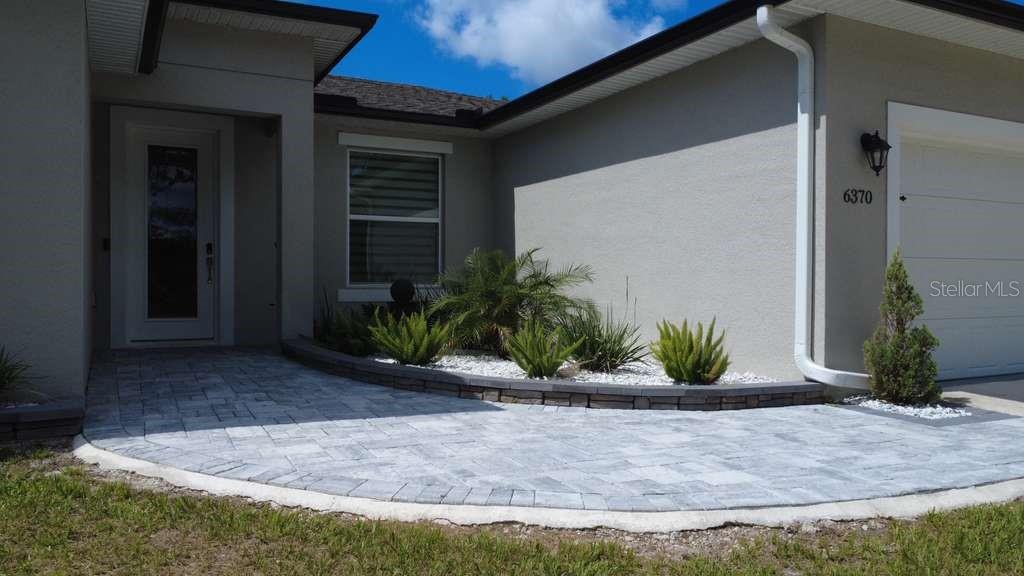 A paved walkway leads to the front entrance of a house with a landscaped garden — 6370 BENNETT COURT, ST CLOUD, FL