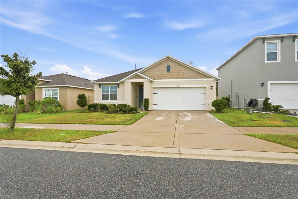 A single-story suburban house with a tan stucco exterior, a two-car garage, and a driveway — 3577 YARIAN DRIVE, HAINES CITY, FL