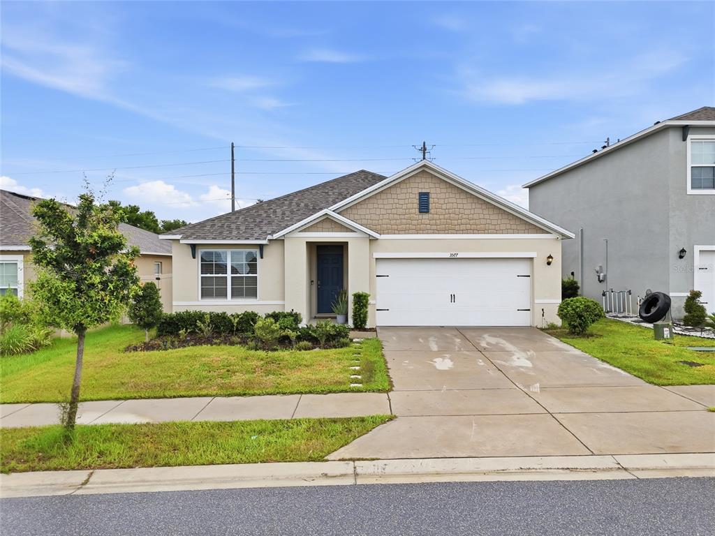 A single-story suburban house with a tan stucco exterior, shingled roof, and two-car garage — 3577 YARIAN DRIVE, HAINES CITY, FL