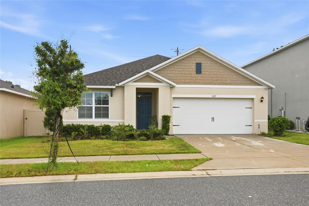 A single-story suburban house with a beige stucco exterior, a two-car garage, and a lawn — 3577 YARIAN DRIVE, HAINES CITY, FL